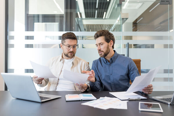 Two business colleagues working together, discussing documents and analyzing data during a corporate meeting in a contemporary office setting, demonstrating teamwork and partnership